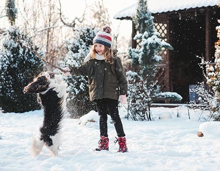 Mädchen spielt mit einem kleinen Hund im Schnee